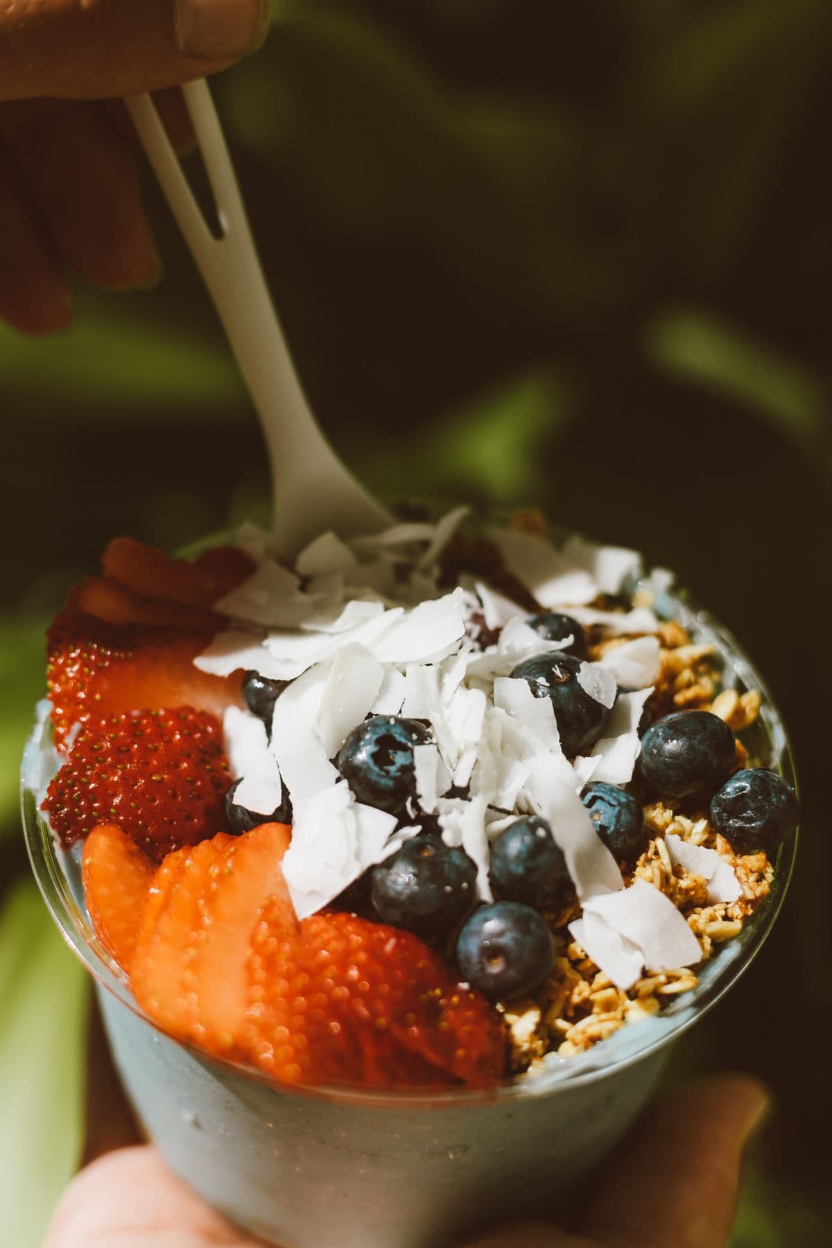 Vaso de açaí sostenido en la mano, con coco y arándano